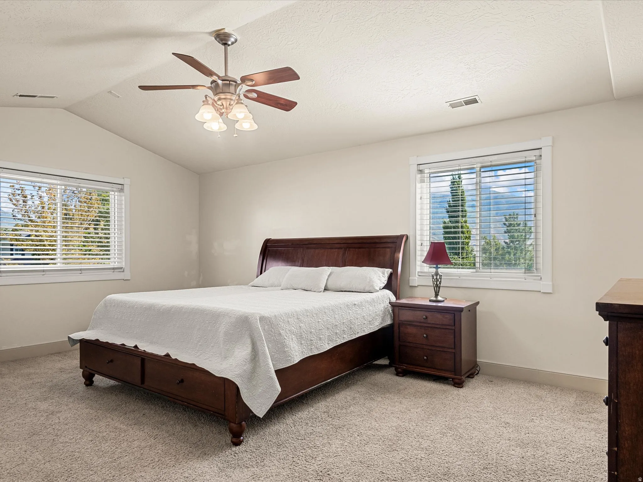Vaulted ceiling with a ceiling fan, dual windows, and plush carpeting