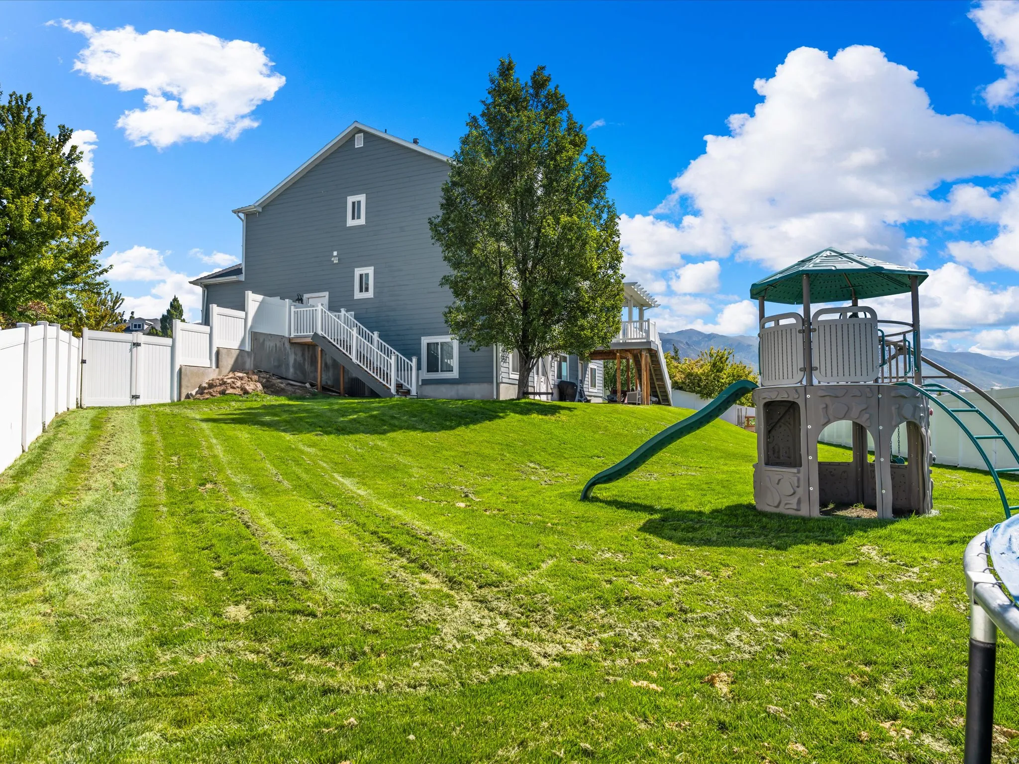 Expansive grassy yard with a multi-level deck and white privacy fencing