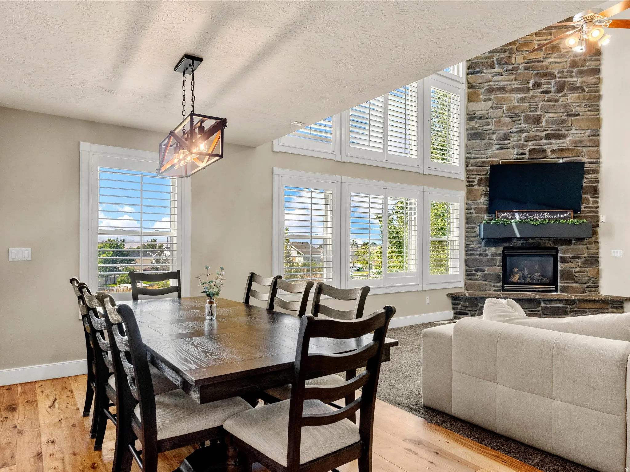Hardwood-finish flooring, a contemporary chandelier, a stone-clad fireplace with a gas insert, and multiple windows with plantation shutters
