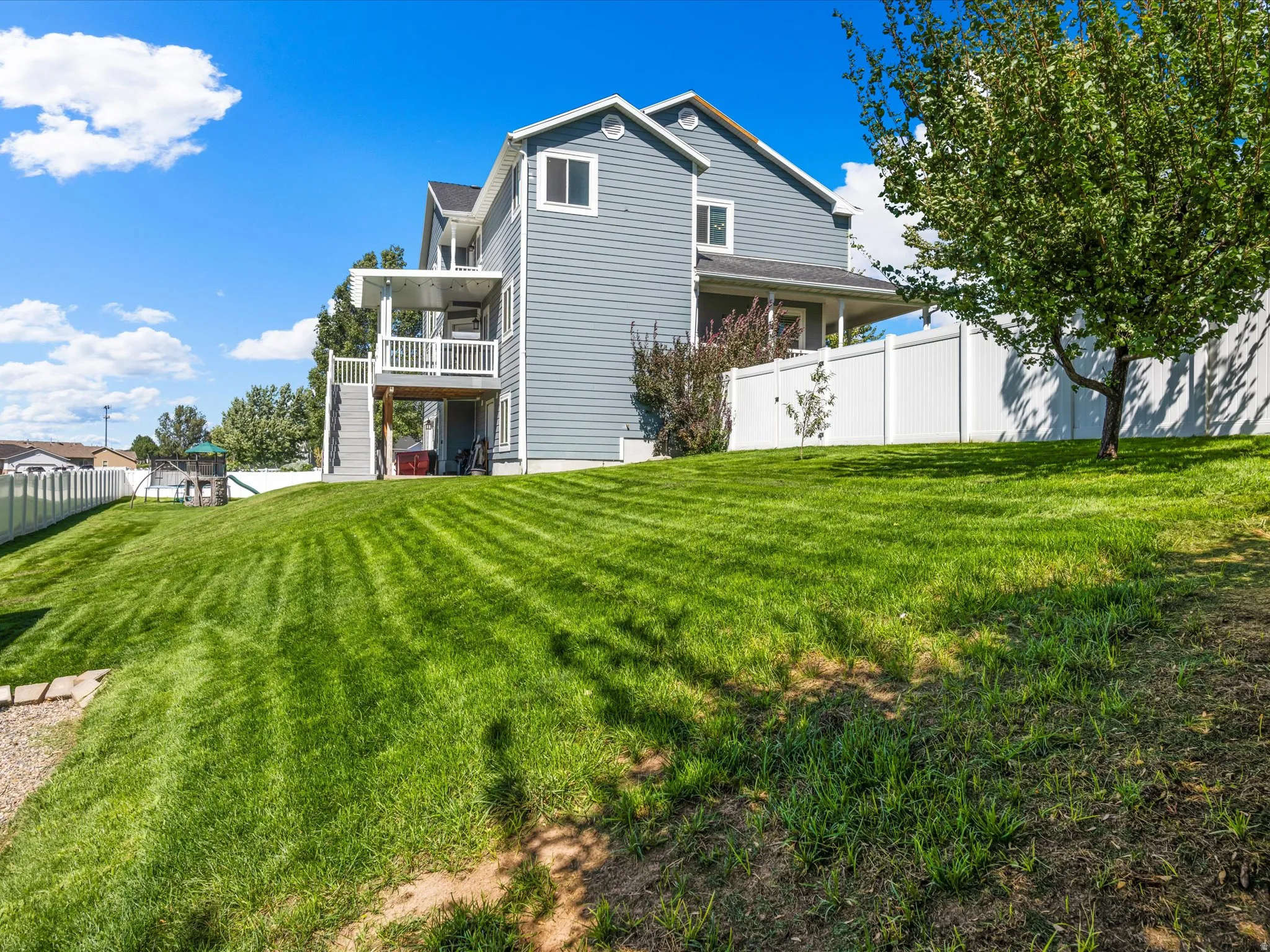 Expansive sloped lawn with mature tree and privacy fencing