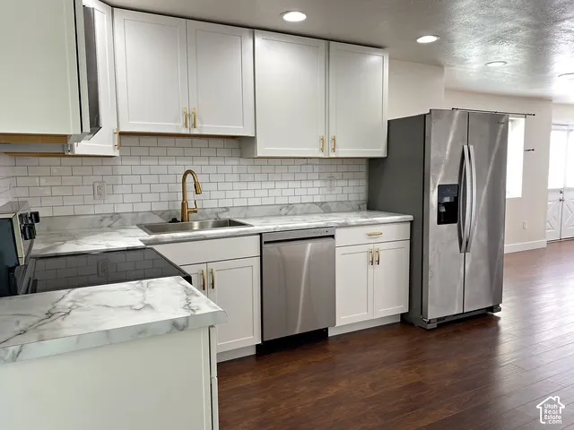 White shaker cabinetry, stainless steel appliances, wood-finish flooring, white subway tile backsplash, and a gold-finish faucet