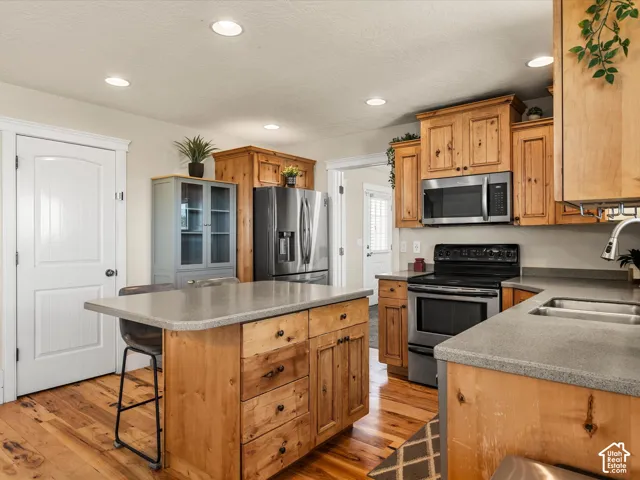 Kitchen featuring wood-finish cabinetry, stainless steel appliances, a center island with a grey countertop, recessed lighting, and wood-finish flooring