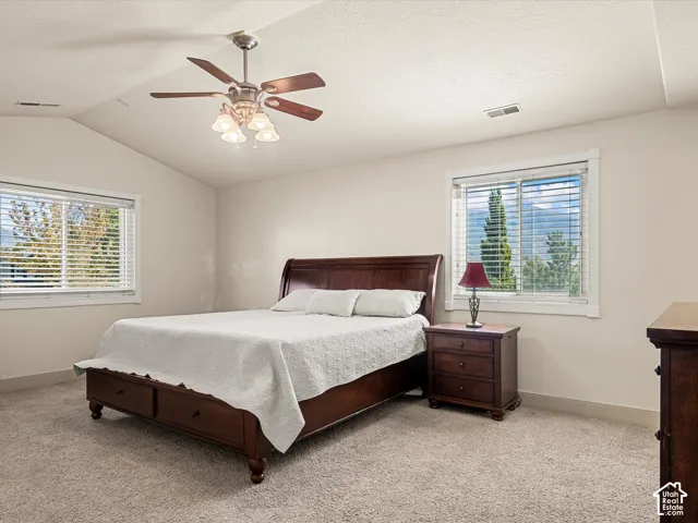 Vaulted ceiling with a ceiling fan, dual windows, and plush carpeting