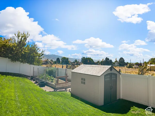 Expansive backyard featuring a manicured lawn, white privacy fencing, a storage shed, and a raised garden bed