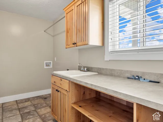 Utility room with wood-finish cabinetry, a built-in sink, and a window with blinds