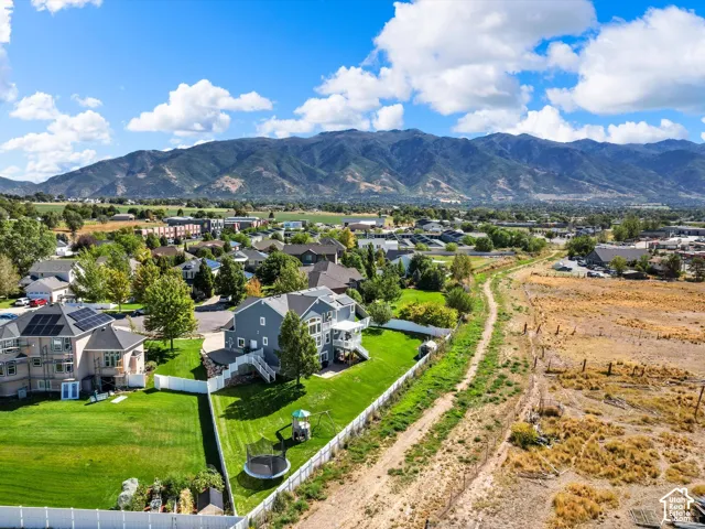 Expansive property featuring a multi-story residence with a gray exterior, a spacious green lawn, a white perimeter fence, and mountain scenery in the background