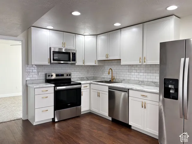 Contemporary kitchen featuring white cabinetry, stainless steel appliances, light-toned countertops, subway tile backsplash, and dark wood-finish flooring