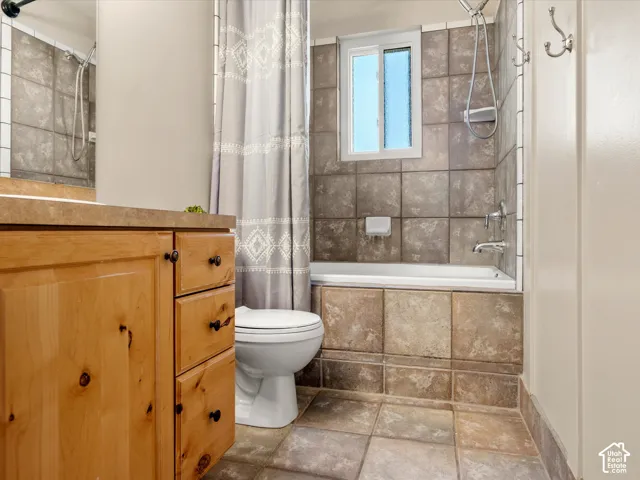 Wood-finish vanity with countertop, tiled flooring, tiled bath and shower surround, and a white framed window