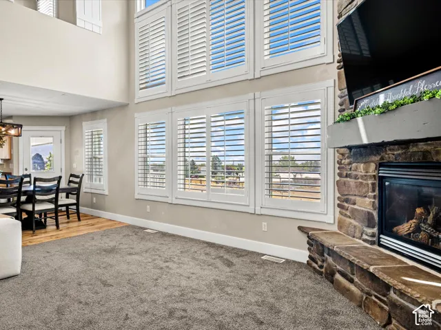 Floor-to-ceiling windows with white plantation shutters, stone-clad fireplace with hearth seating, wood-finish flooring, and recessed lighting