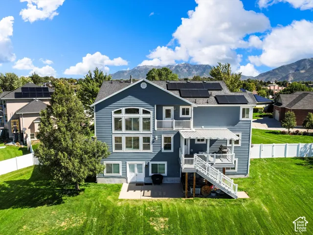 Blue siding exterior with multiple solar panels, a multi-level deck with white railings, and a lower-level patio