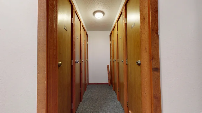 Hallway with multiple wood-finish doors, textured walls, and overhead lighting
