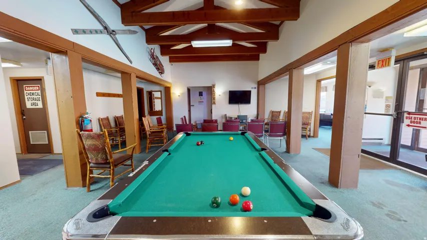 Expansive recreation area featuring a billiard table, wood-beam ceiling, exposed structural wood elements, and recessed lighting