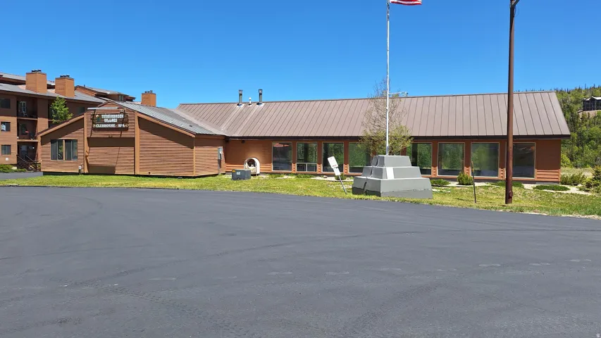 Wood-paneled facade with a brown metal roof, featuring multiple large windows and a paved parking area