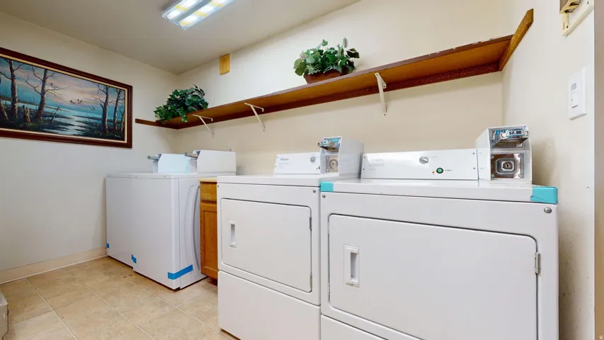 Laundry area featuring multiple white laundry machines, wood-finish cabinetry, and tiled flooring