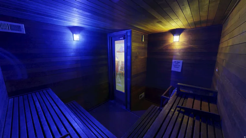 Wood-paneled room featuring built-in slatted benches, wall-mounted light fixtures, and a glass-paneled door