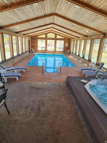 Indoor swimming pool with an integrated hot tub, wood-paneled vaulted ceiling, and multiple large windows