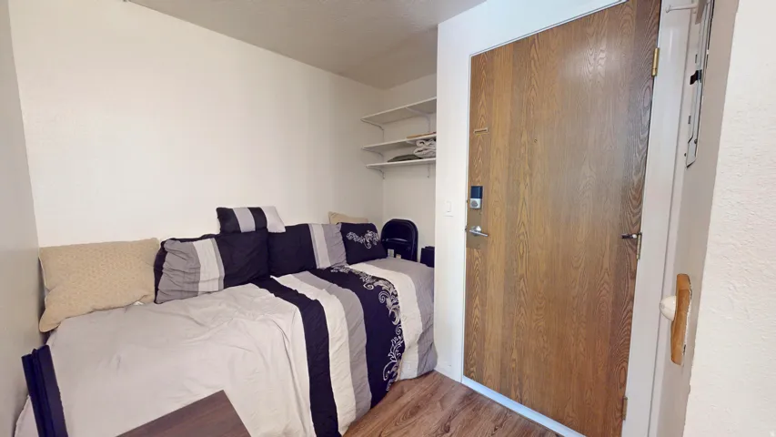 Wood-finish entry door with modern hardware, accompanied by built-in shelving and wood-finish flooring