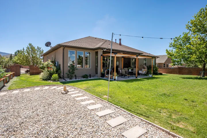 Expansive backyard with a covered patio, pergola, concrete paver patio, gravel pathway with stepping stones, and raised garden beds