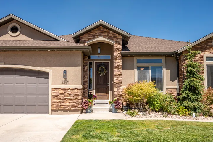 Stone veneer accents, stucco exterior, covered entry, attached garage, and mature landscaping