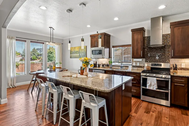 Kitchen featuring wood-finish flooring, dark wood cabinetry, stainless steel appliances, granite countertops, and a large island with pendant lighting