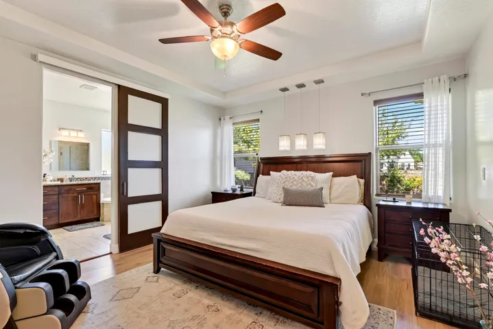 Tray ceiling, wood-finish flooring, two large windows, sliding barn door, and a ceiling fan with integrated lighting