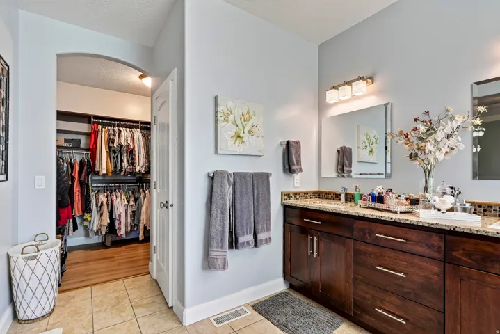 Dual vanity with granite countertop, integrated sinks, wood cabinetry, and tiled flooring