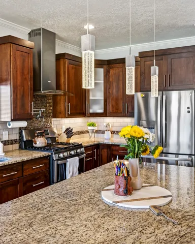 Kitchen featuring wood cabinetry, stainless steel appliances, speckled stone countertops, a tile backsplash, and overhead pendant lighting