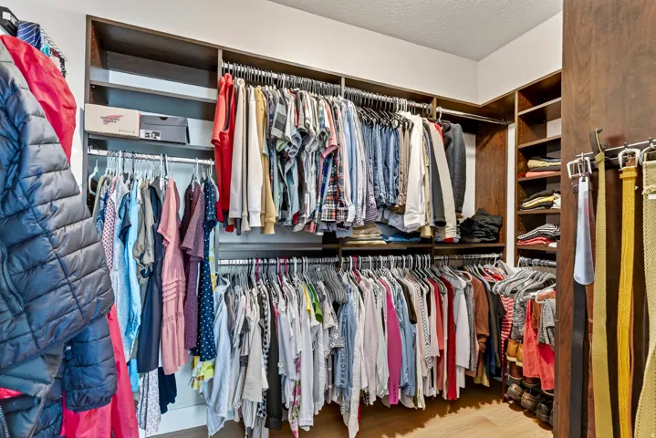 Custom closet organization system with multiple hanging rods, built-in shelving, wood-finish cabinetry, and corner storage