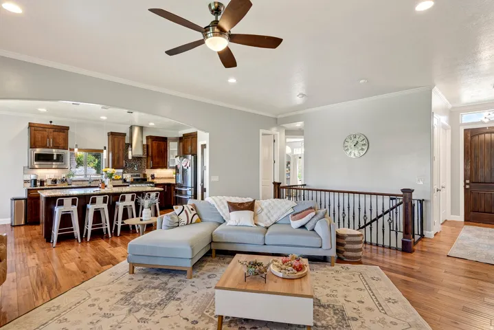 Hardwood-finish flooring throughout, kitchen with wood cabinetry, stainless steel appliances, and island seating, a ceiling fan with integrated lighting, and a wrought iron banister