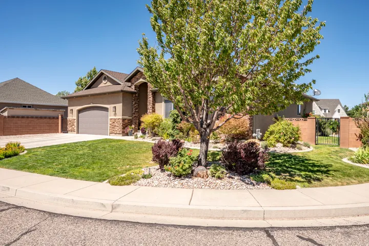 Stucco and stone exterior with an attached garage, paved driveway, and mature landscaping