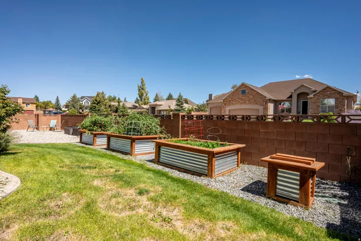 Expansive backyard with a manicured lawn, a gravel patio, and multiple raised garden beds with corrugated metal and wood-finish framing