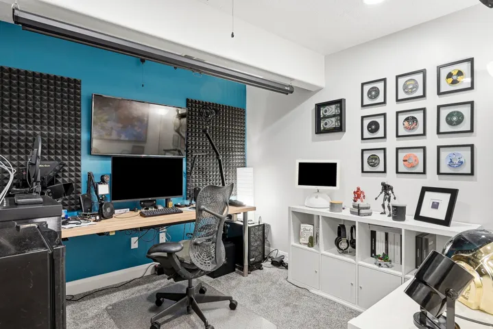 Built-in desk with a wood-finish surface, accent wall, wall-mounted sound dampening panels, track lighting, and soft grey carpeting