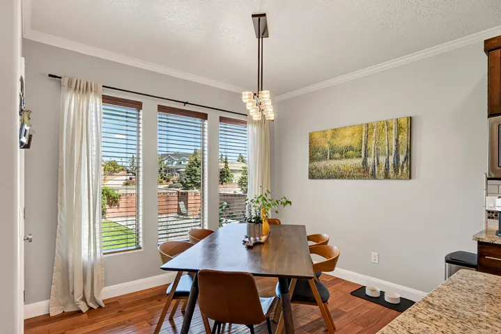 Wood-finish flooring, crown molding, and a contemporary linear chandelier with frosted glass shades