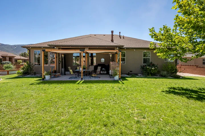 Expansive green lawn, stucco exterior, covered patio with pergola, and visible mountain backdrop