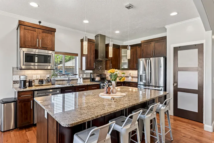 Kitchen featuring dark wood cabinetry, stainless steel appliances, granite island, tile backsplash, and wood-finish flooring