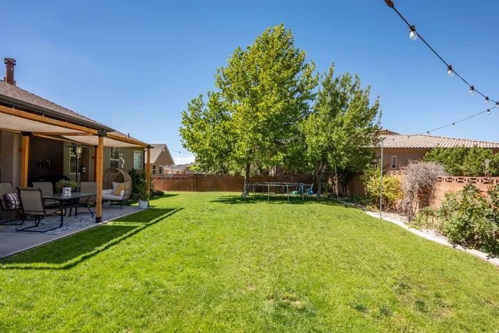 Expansive backyard featuring a manicured lawn, established trees, and a concrete patio with a wooden pergola