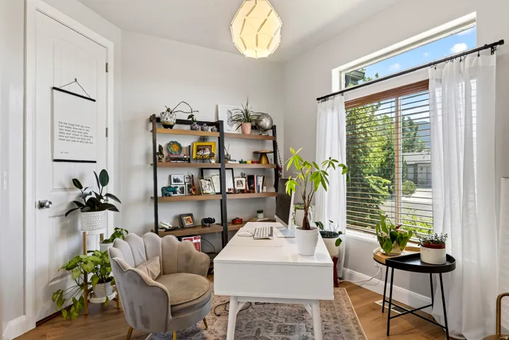 Wood-finish flooring, white paneled door, built-in shelving with wood and metal construction, large window with blinds and sheer curtains, and a distinctive geometric ceiling light fixture