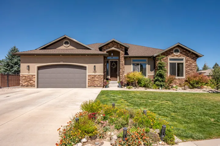 Stucco and stone facade with a gable roof, an integrated garage, a concrete driveway, and established landscaping