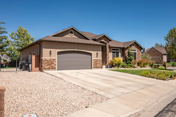 Stucco and stone exterior featuring a multi-car garage, concrete driveway, and landscaped front yard with shrubs and trees