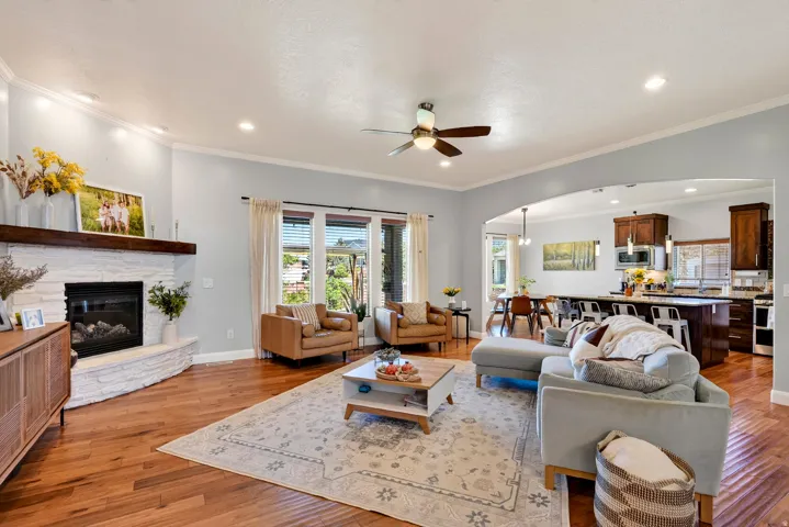 Open concept living space featuring wood-finish flooring, a stone-clad fireplace with wood mantel, recessed lighting, and a ceiling fan