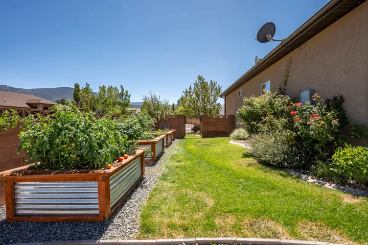 Landscaped backyard featuring raised garden beds with wood frames and corrugated metal, a manicured lawn, and lush plantings along the stucco exterior
