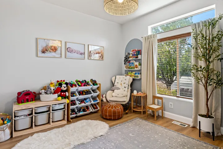 Large window with blinds and drapes, wood-finish flooring, built-in shelving, and a woven ceiling light fixture