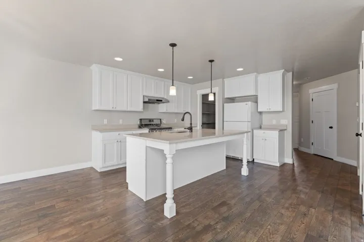 Kitchen featuring wood-finish flooring, white cabinetry, a center island with pendant lighting, a gas range, and a built-in microwave