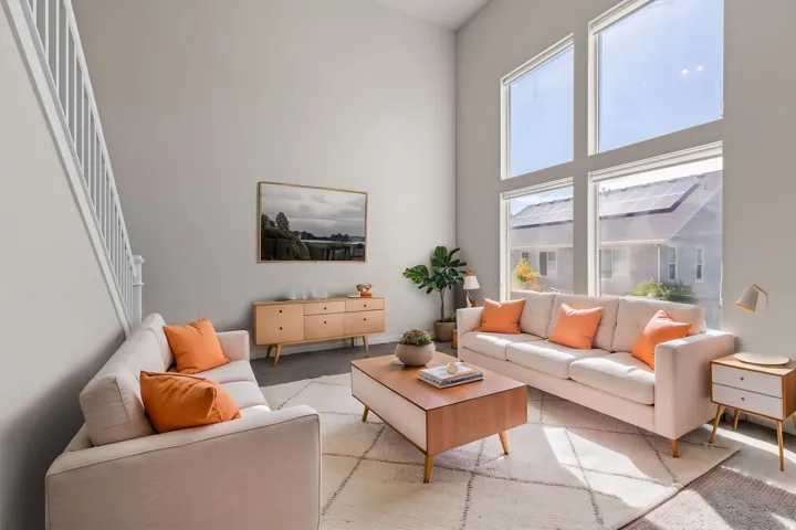 Two-story ceiling, large multi-pane windows, staircase with white railing, light-toned walls, and wood-finish flooring