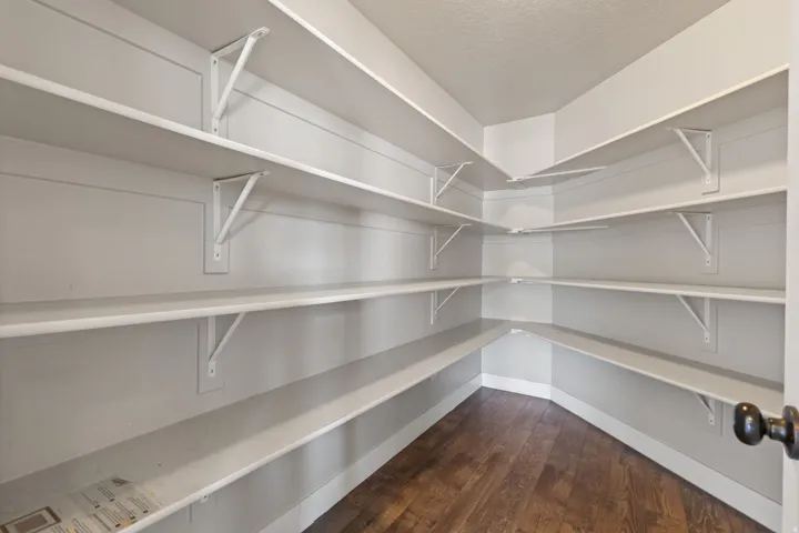 Corner pantry featuring extensive white shelving and wood-finish flooring