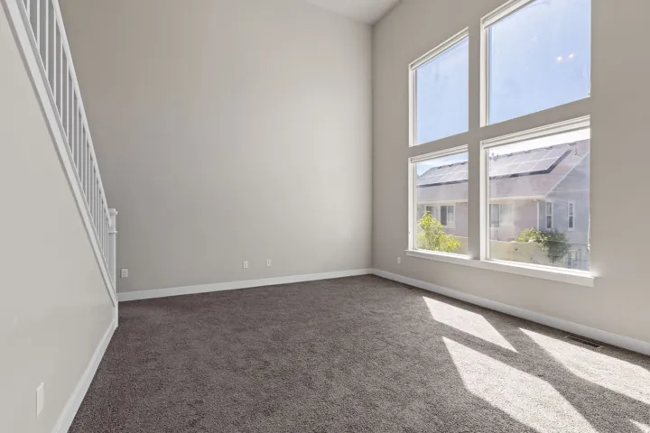 Expansive interior with high ceilings, multiple large windows, soft gray wall paint, white stair railing, and neutral-toned carpeting