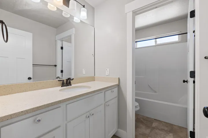 White shaker-style vanity with a light-toned countertop, under-mount sink, and dark-finish faucet
