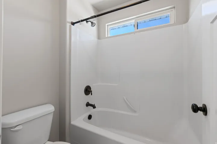 White tub and shower combination with oil-rubbed bronze fixtures, transom window, and white toilet