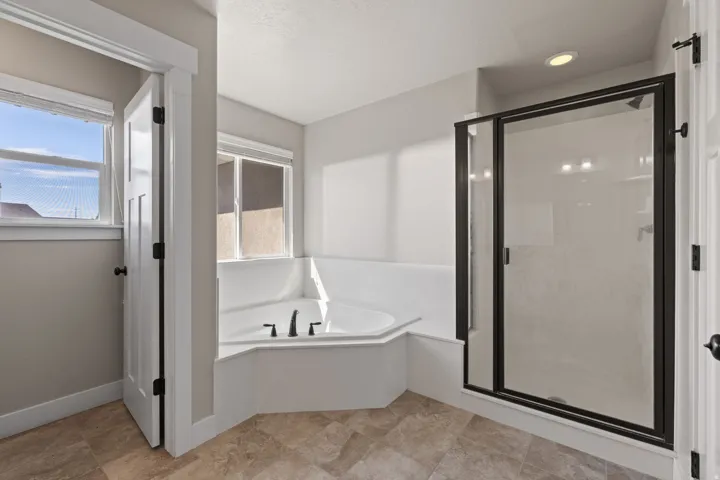 Corner soaking tub with matte black fixtures, an enclosed shower with a black frame, and tiled flooring