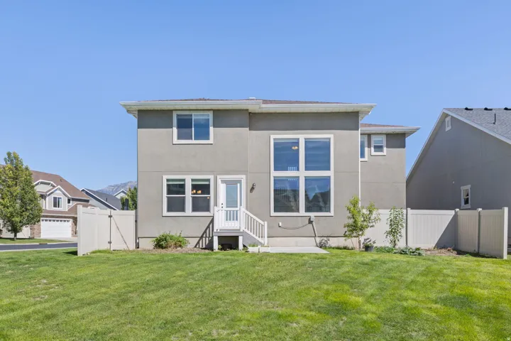 Expansive backyard featuring a manicured lawn, two-story exterior with stucco finish, white frame windows, a ground-level patio door, and a white privacy fence